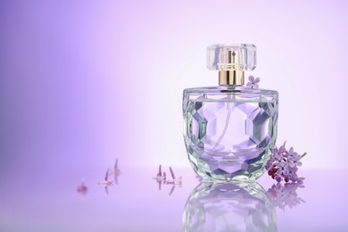 Photo of Beautiful lilac flowers and perfume on mirror surface against violet gradient background, space for text