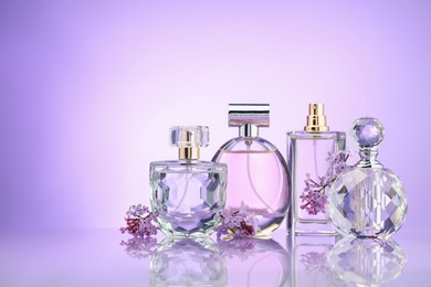 Photo of Bottles of perfume and lilac flowers on mirror surface against violet gradient background, space for text
