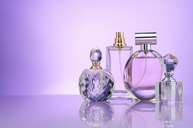 Photo of Bottles of perfume on mirror surface against violet gradient background, space for text