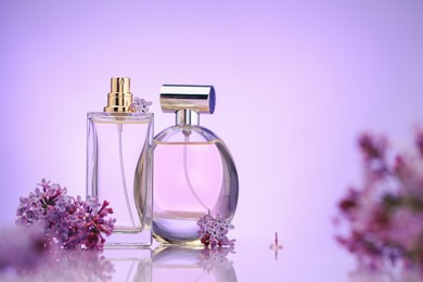 Photo of Bottles of perfume and lilac flowers on mirror surface against violet gradient background, selective focus. Space for text