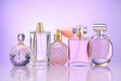 Photo of Bottles of perfume on mirror surface against violet gradient background