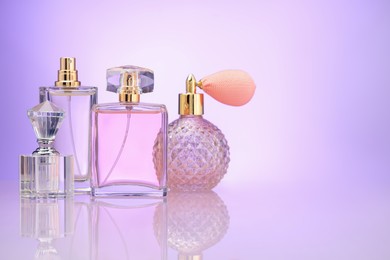 Photo of Bottles of perfume on mirror surface against violet gradient background, space for text