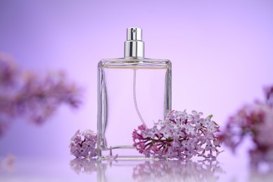 Photo of Bottle of perfume and lilac flowers on mirror surface against violet gradient background, selective focus