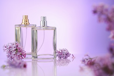 Photo of Bottles of perfume and lilac flowers on mirror surface against violet gradient background, selective focus