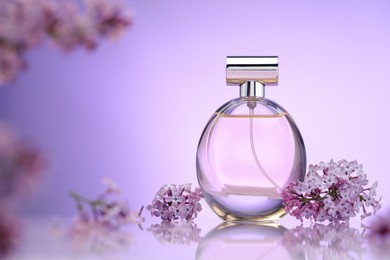 Photo of Bottle of perfume and lilac flowers on mirror surface against violet gradient background, selective focus