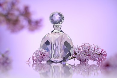 Photo of Bottle of perfume and lilac flowers on mirror surface against violet gradient background, selective focus