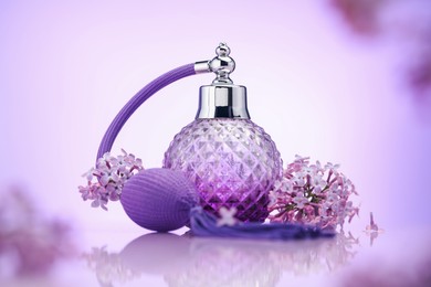 Photo of Bottle of perfume and lilac flowers on mirror surface against violet gradient background, selective focus