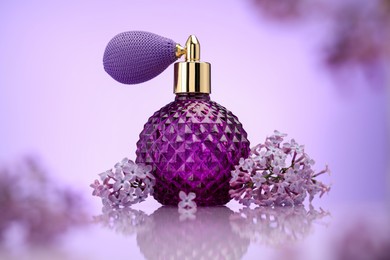 Photo of Bottle of perfume and lilac flowers on mirror surface against violet gradient background, selective focus