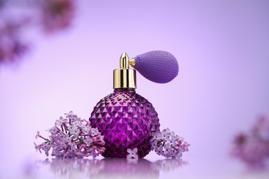 Photo of Bottle of perfume and lilac flowers on mirror surface against violet gradient background, selective focus