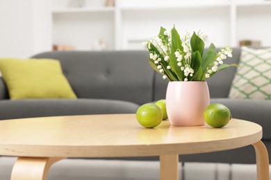 Photo of Bouquet of beautiful lily-of-the-valley and limes on coffee table indoors