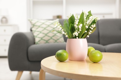Photo of Bouquet of beautiful lily-of-the-valley and limes on coffee table indoors. Space for text