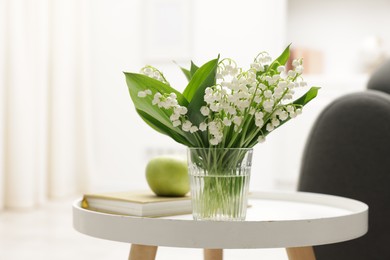 Photo of Bouquet of beautiful lily-of-the-valley on coffee table indoors