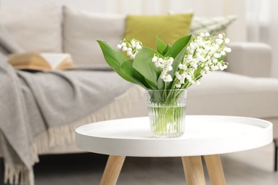 Photo of Bouquet of beautiful lily-of-the-valley on coffee table indoors