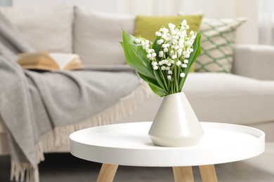 Photo of Bouquet of beautiful lily-of-the-valley in vase on coffee table indoors