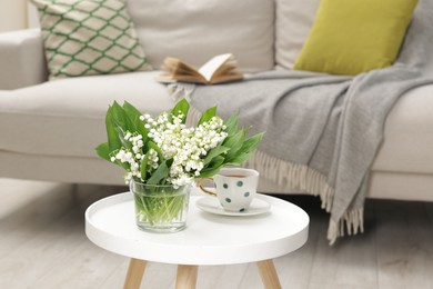 Photo of Bouquet of beautiful lily-of-the-valley and cup of tea on coffee table indoors