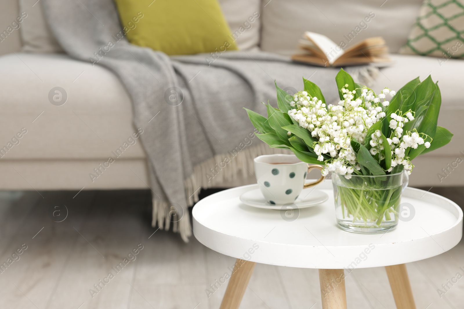 Bouquet of beautiful lily-of-the-valley and cup of tea on coffee table indoors. Space for text Photo of Bouquet of beautiful lily-of-the-valley and cup of tea on coffee table indoors. Space for text