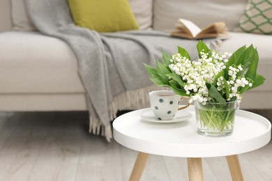 Photo of Bouquet of beautiful lily-of-the-valley and cup of tea on coffee table indoors. Space for text