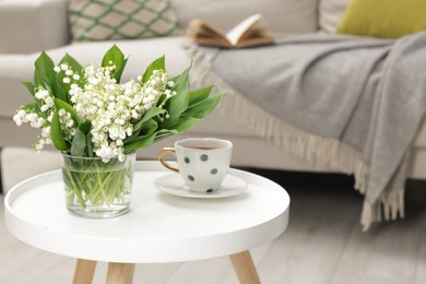 Photo of Bouquet of beautiful lily-of-the-valley and cup of tea on coffee table indoors
