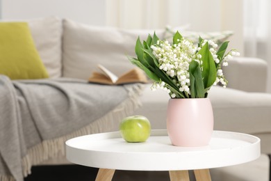 Photo of Bouquet of beautiful lily-of-the-valley and apple on coffee table indoors