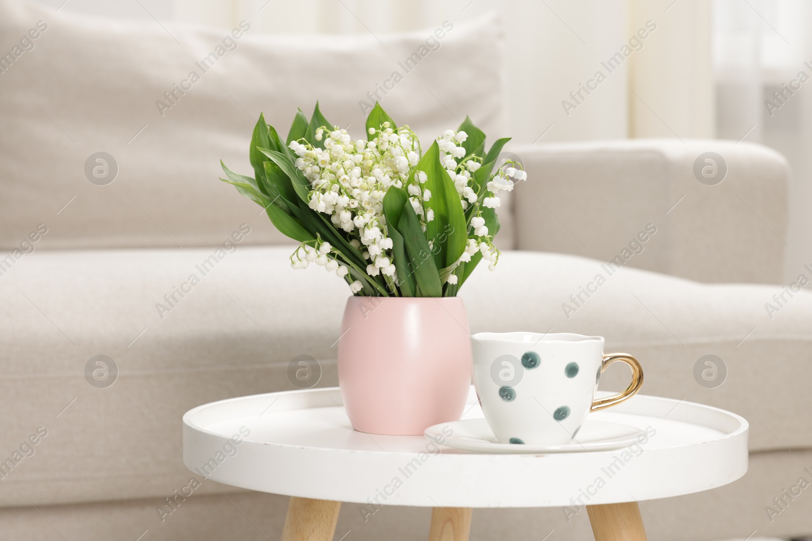 Bouquet of beautiful lily-of-the-valley and cup on coffee table indoors Photo of Bouquet of beautiful lily-of-the-valley and cup on coffee table indoors