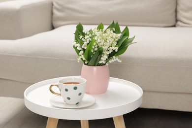 Photo of Bouquet of beautiful lily-of-the-valley and cup of tea on coffee table indoors