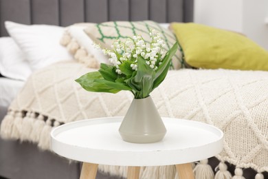 Photo of Bouquet of beautiful lily-of-the-valley in vase on coffee table indoors