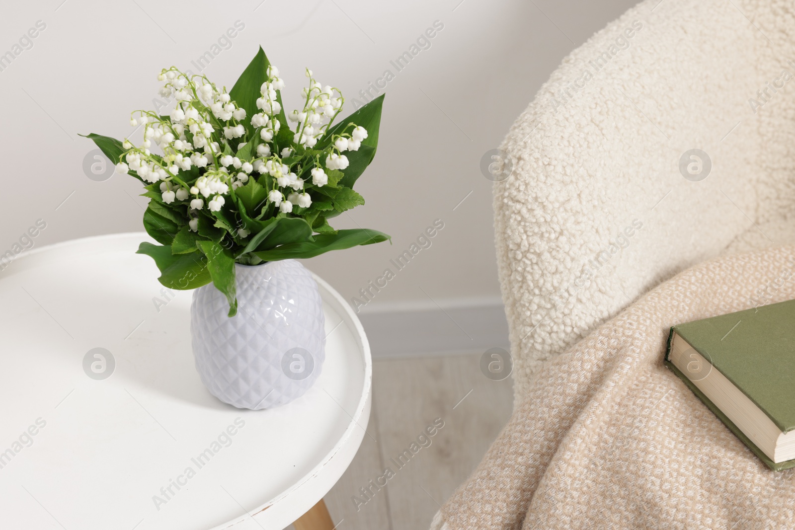 Bouquet of beautiful lily-of-the-valley in vase on coffee table near armchair indoors Photo of Bouquet of beautiful lily-of-the-valley in vase on coffee table near armchair indoors