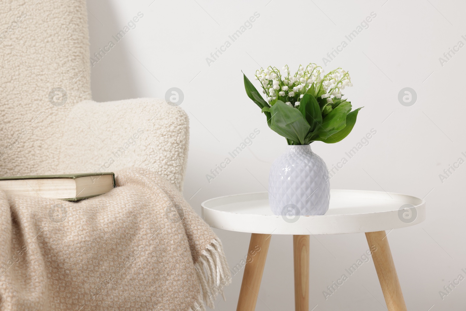 Bouquet of beautiful lily-of-the-valley in vase on coffee table near armchair indoors Photo of Bouquet of beautiful lily-of-the-valley in vase on coffee table near armchair indoors