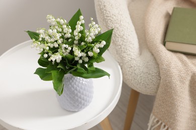 Photo of Bouquet of beautiful lily-of-the-valley in vase on coffee table near armchair indoors