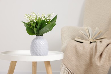 Photo of Bouquet of beautiful lily-of-the-valley in vase on coffee table indoors