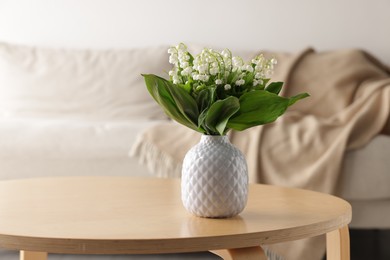 Photo of Bouquet of beautiful lily-of-the-valley in vase on coffee table indoors