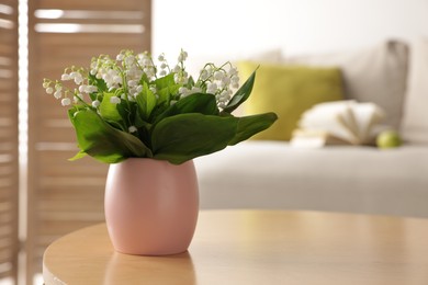 Photo of Bouquet of beautiful lily-of-the-valley on coffee table indoors