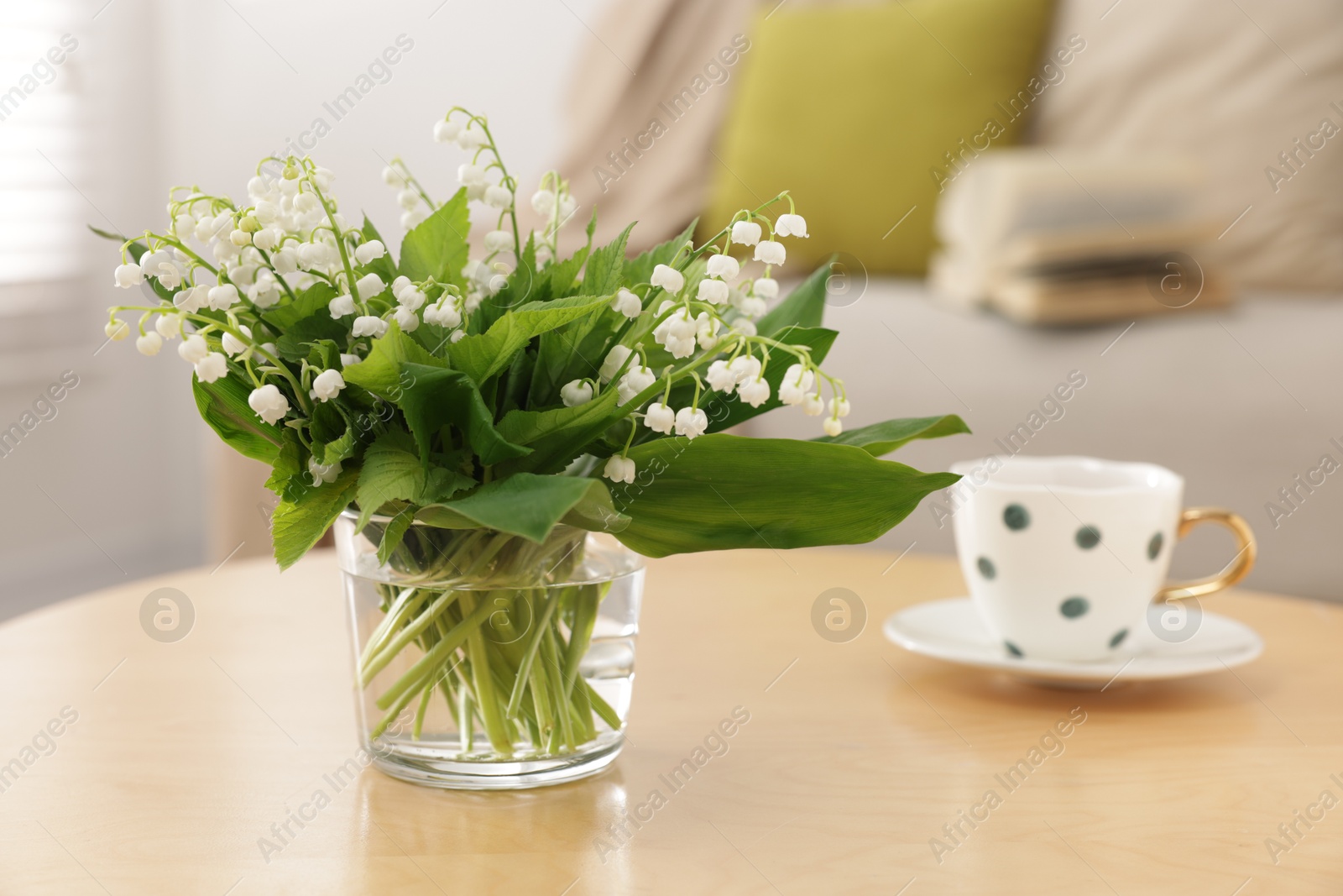 Bouquet of beautiful lily-of-the-valley and cup on table indoors, closeup Photo of Bouquet of beautiful lily-of-the-valley and cup on table indoors, closeup