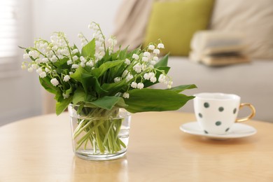 Photo of Bouquet of beautiful lily-of-the-valley and cup on table indoors, closeup