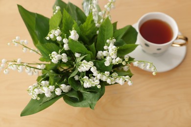 Photo of Bouquet of beautiful lily-of-the-valley and cup of tea on wooden table, closeup