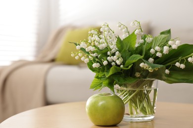 Photo of Bouquet of beautiful lily-of-the-valley and apple on table indoors, closeup. Space for text