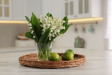 Photo of Bouquet of beautiful lily-of-the-valley and limes on white marble table in kitchen