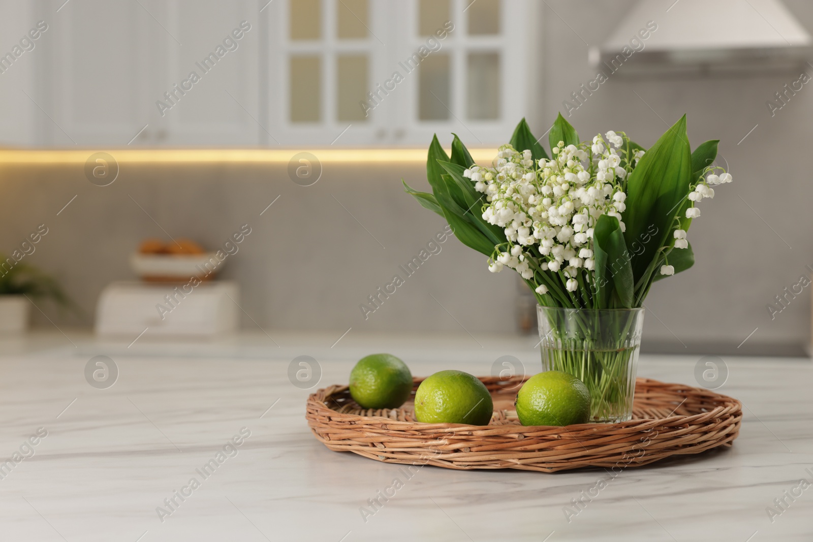 Bouquet of beautiful lily-of-the-valley and limes on white marble table in kitchen. Space for text Photo of Bouquet of beautiful lily-of-the-valley and limes on white marble table in kitchen. Space for text