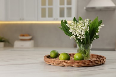 Photo of Bouquet of beautiful lily-of-the-valley and limes on white marble table in kitchen. Space for text
