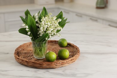 Photo of Bouquet of beautiful lily-of-the-valley and limes on white marble table
