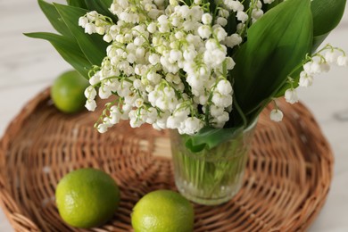 Photo of Bouquet of beautiful lily-of-the-valley and limes on white table, closeup