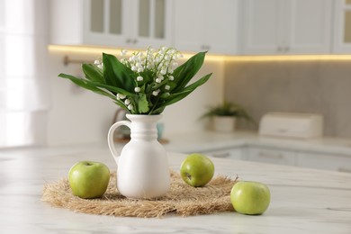 Photo of Bouquet of beautiful lily-of-the-valley in vase and apples on white marble table in kitchen