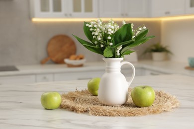 Photo of Bouquet of beautiful lily-of-the-valley in vase and apples on white marble table in kitchen