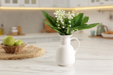 Photo of Bouquet of beautiful lily-of-the-valley in vase and apples on white marble table in kitchen