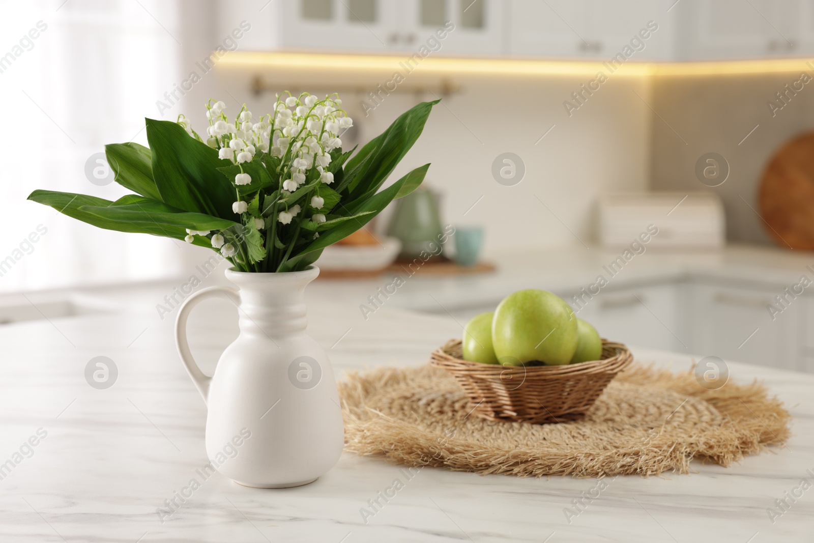 Bouquet of beautiful lily-of-the-valley in vase and apples on white marble table in kitchen Photo of Bouquet of beautiful lily-of-the-valley in vase and apples on white marble table in kitchen