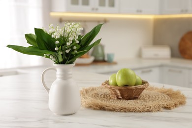 Photo of Bouquet of beautiful lily-of-the-valley in vase and apples on white marble table in kitchen