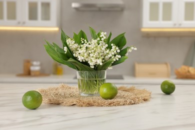 Photo of Bouquet of beautiful lily-of-the-valley and limes on white marble table in kitchen