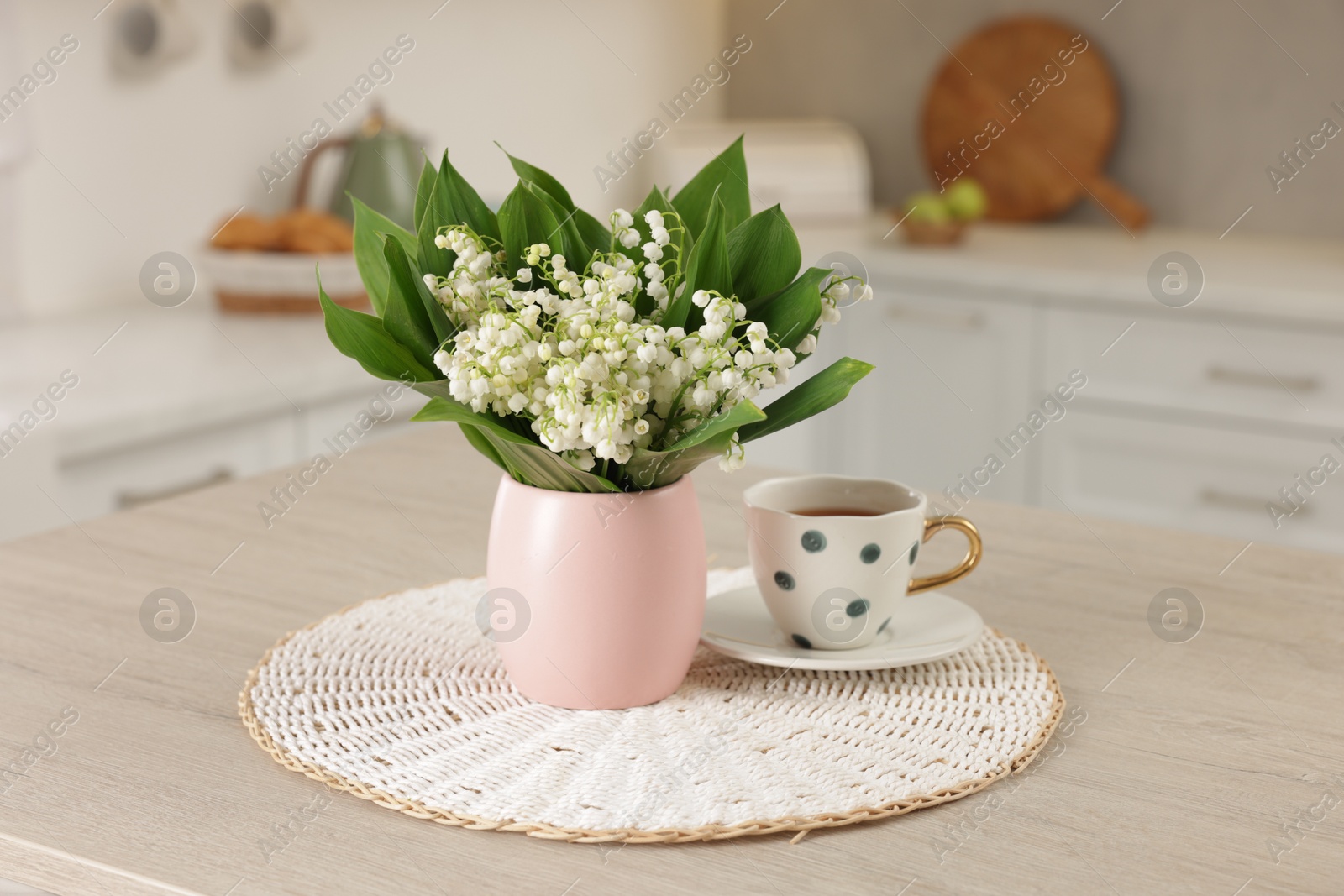 Bouquet of beautiful lily-of-the-valley and cup on wooden table in kitchen Photo of Bouquet of beautiful lily-of-the-valley and cup on wooden table in kitchen
