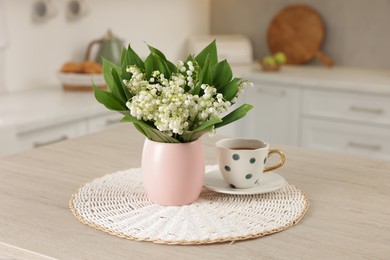 Photo of Bouquet of beautiful lily-of-the-valley and cup on wooden table in kitchen
