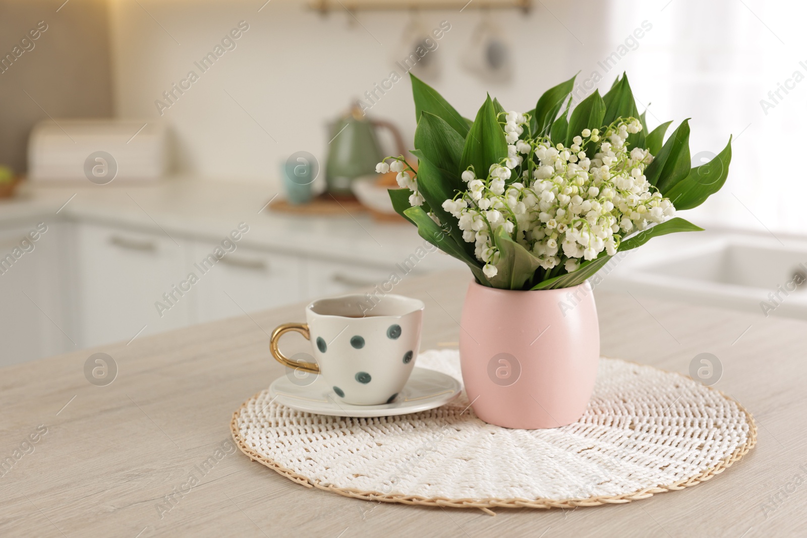 Bouquet of beautiful lily-of-the-valley and cup on wooden table in kitchen Photo of Bouquet of beautiful lily-of-the-valley and cup on wooden table in kitchen